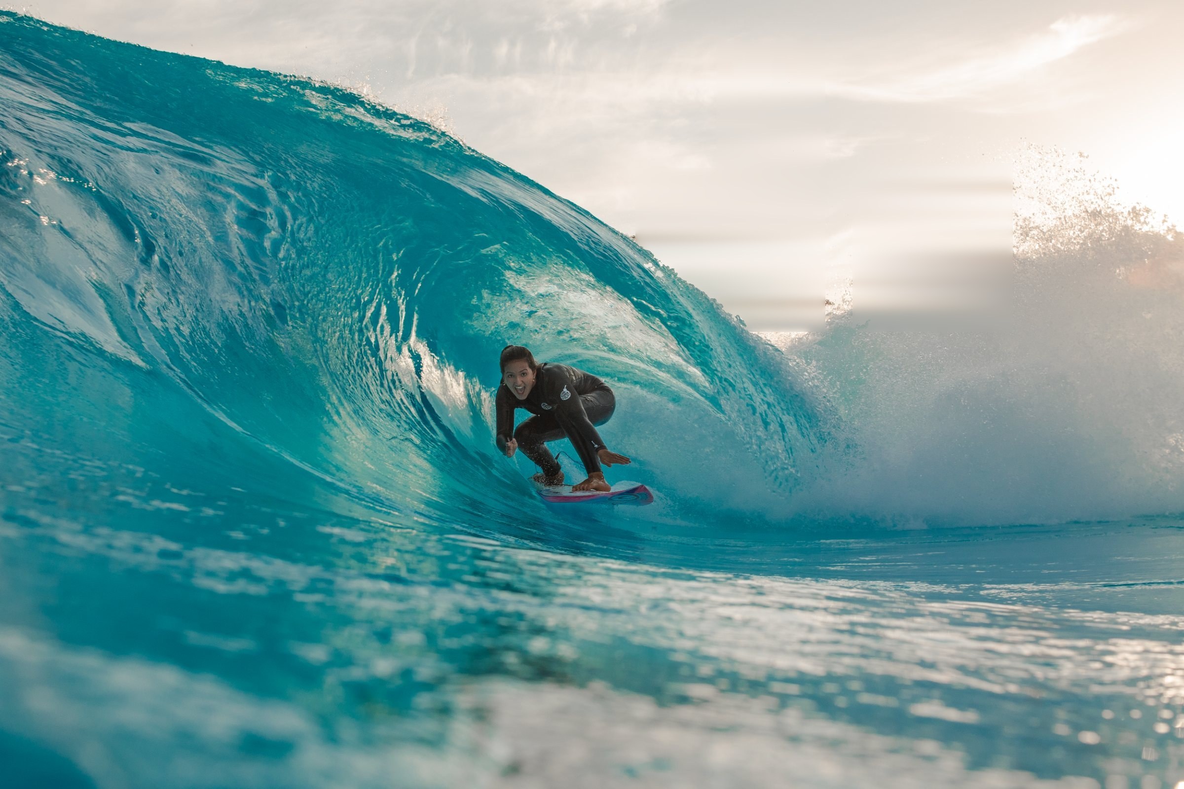 Surfer riding deep inside a turquoise barrel at the surf pool
